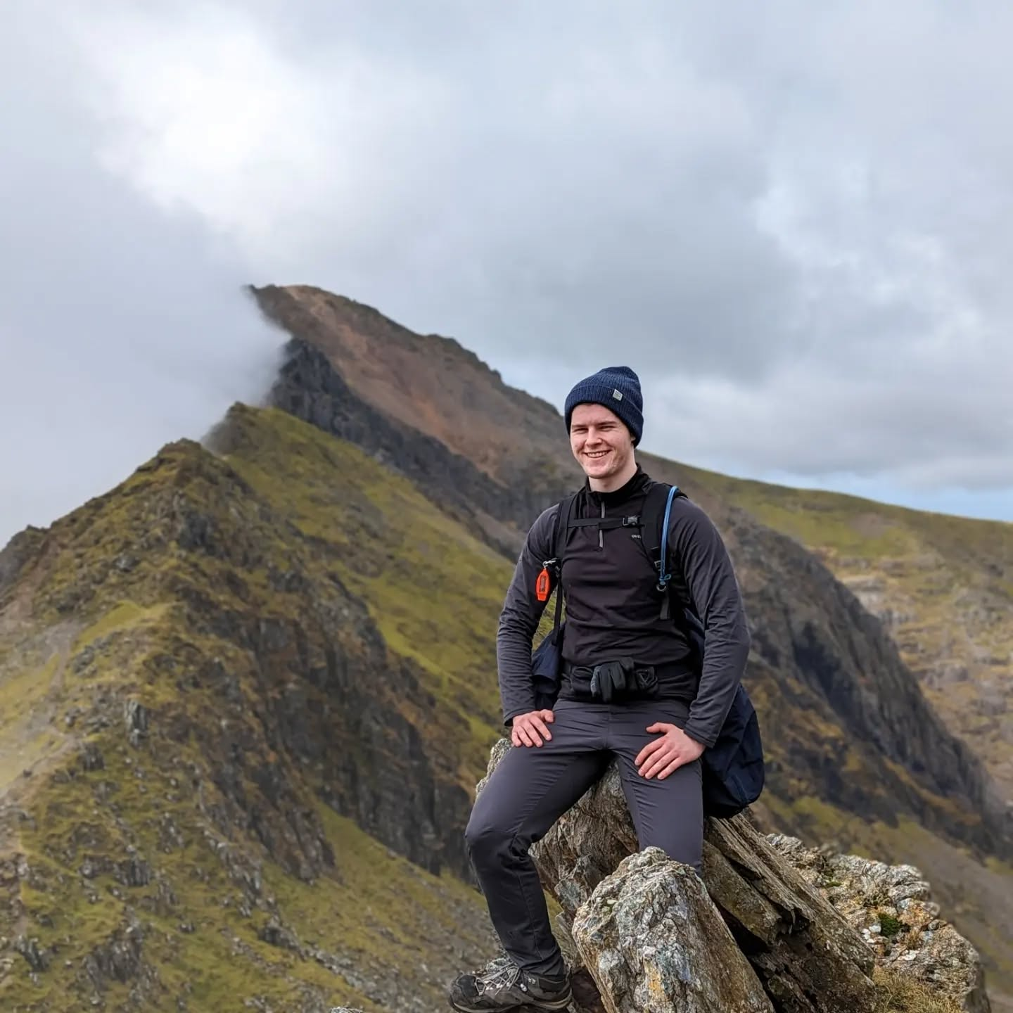 An photo of me hiking on Crib Goch with clouds covering one half of the ridge and clear skies on the other half.